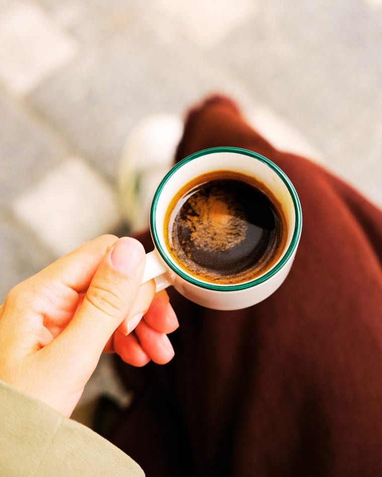 Eine Hand hält eine kleine Espressotasse mit grünem Rand, von oben fotografiert
